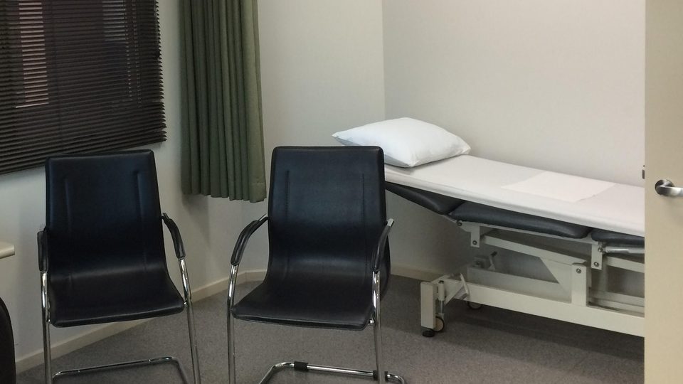 Two black chairs and an examination couch with a white pillow in a quiet consulting room