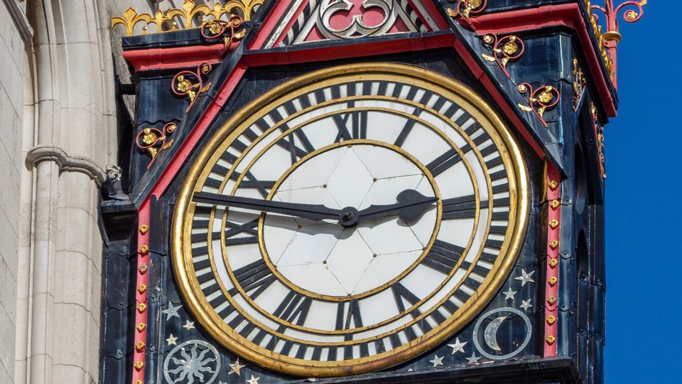The ornate red and gold clock on the Royal Courts of Justice in London against a blue sky