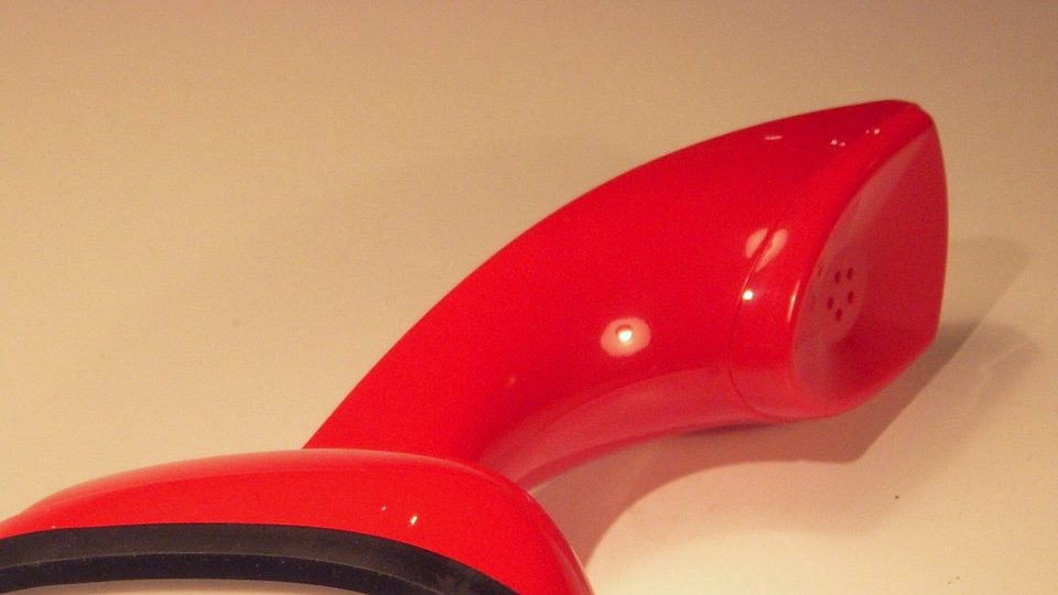The curved glossy red handset of a retro telephone against a warm cream background