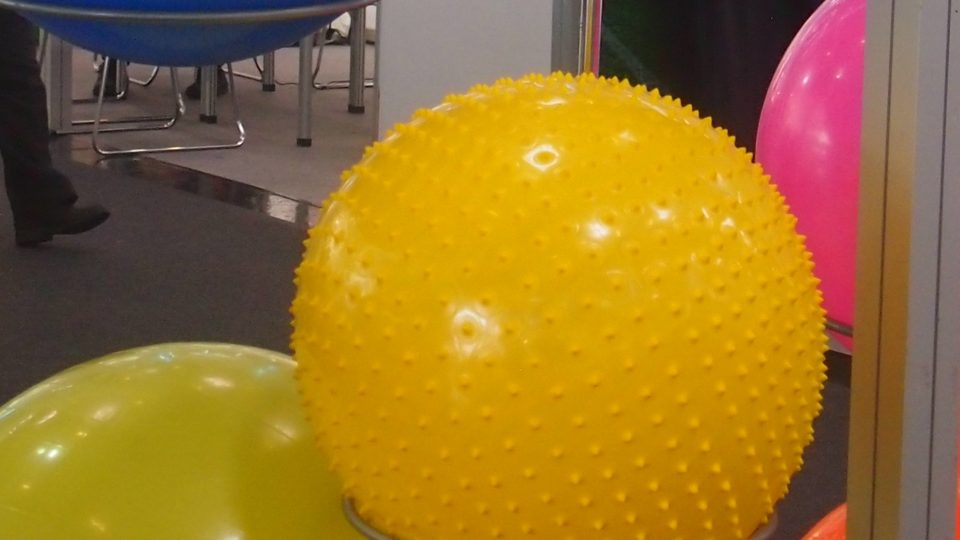 A bright yellow spiked exercise ball on a stand between green, blue and pink exercise balls