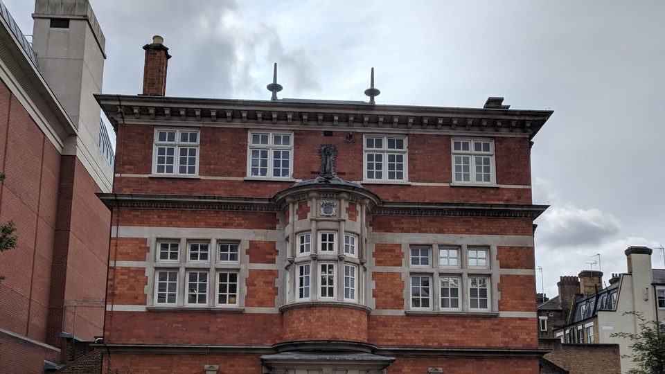 The upper floors of a red brick and stone coroner's court in London, with a bay window and tall chimneys