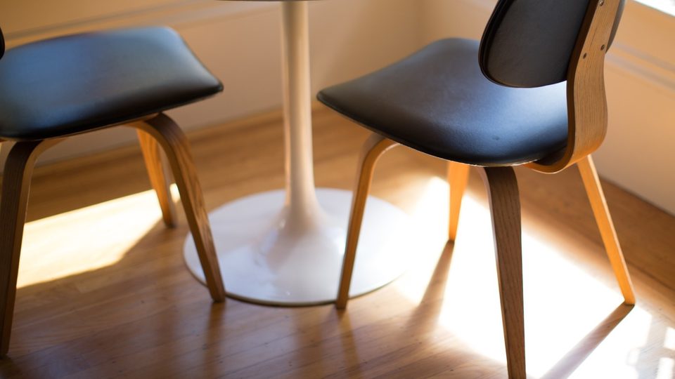 Two wooden chairs with black seats at a white round table in warm afternoon sunlight