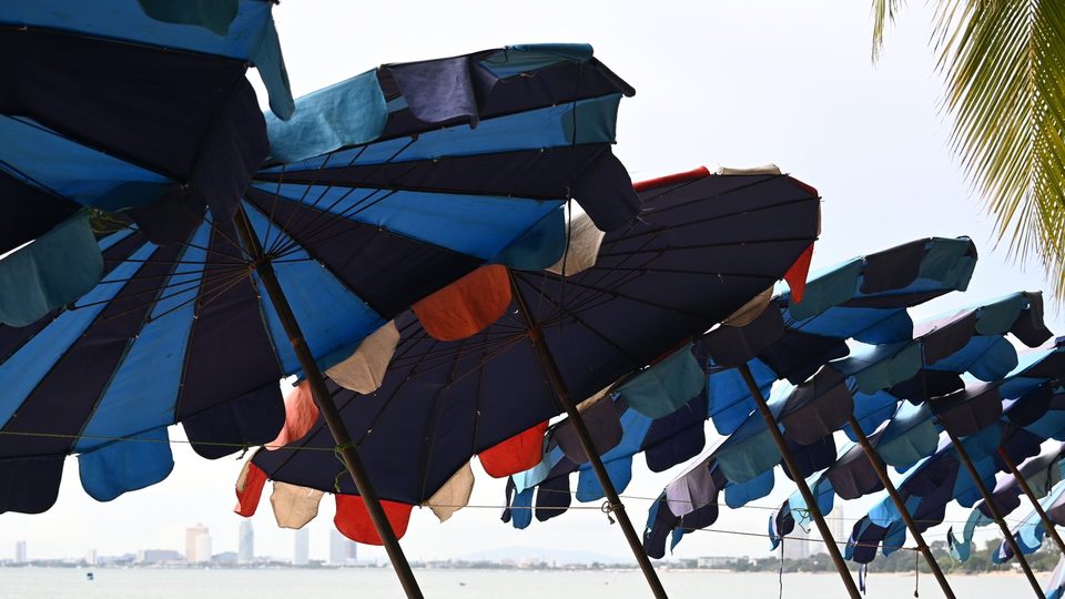 A long row of blue, teal and orange beach umbrellas, each shading its own patch of shore beside the sea