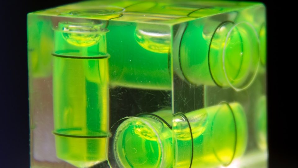 A clear cube spirit level glowing bright green, its bubble vials set on three faces
