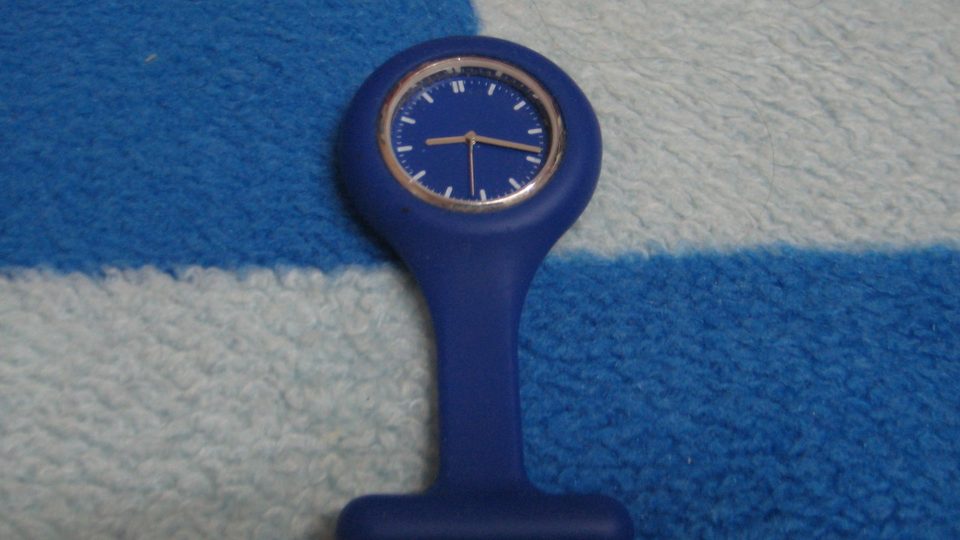 A blue silicone nurse's fob watch with a blue face lying on a blue and white striped fleece