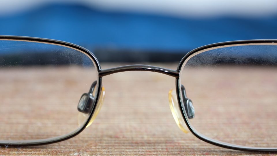 Close view of a pair of metal framed spectacles resting on a wooden surface in front of a blue background