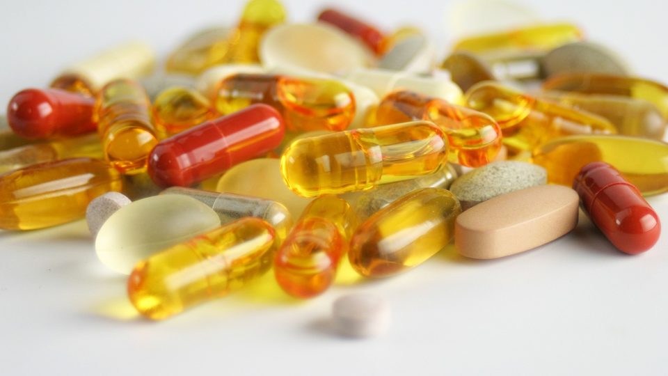 A heap of amber, yellow and red capsules mixed with pale tablets on a white surface