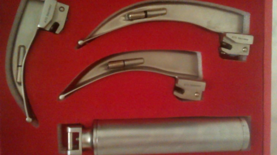 A set of steel laryngoscope blades and a handle resting in a case lined with red velvet