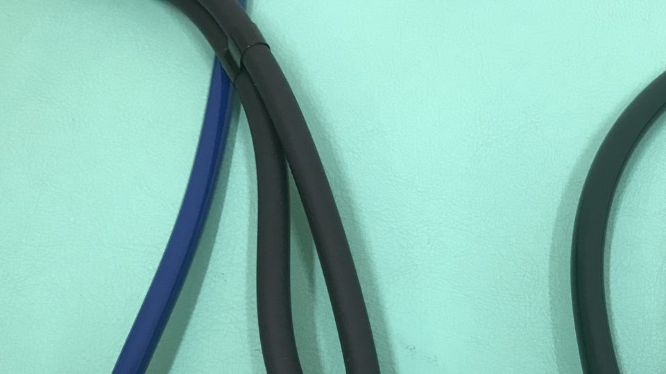 The blue and black tubing of stethoscopes lying on a mint green surface