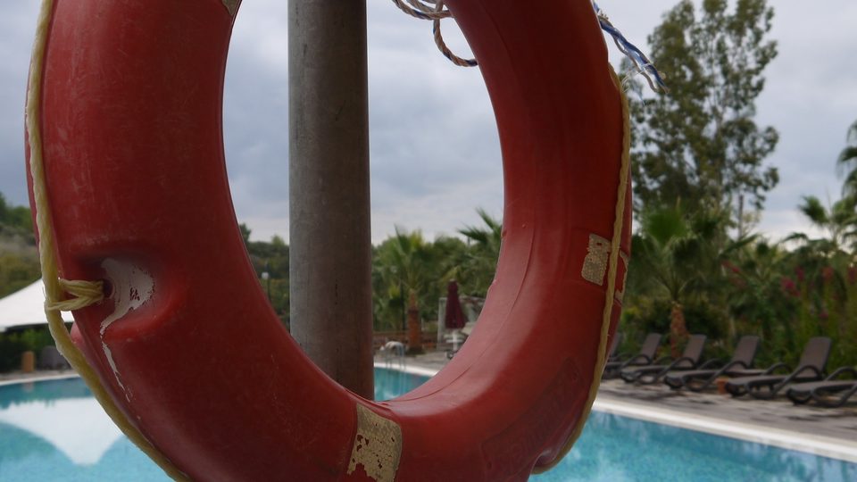 A red lifebuoy hanging from a pole beside a bright blue swimming pool