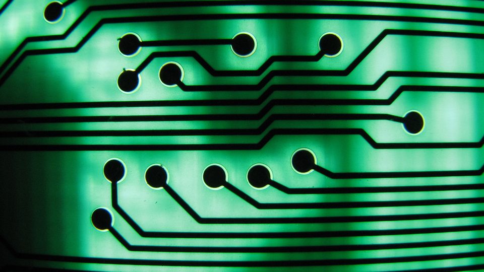 Macro view of copper tracks on a green circuit board lit from behind