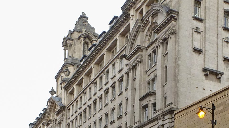 The ornate stone facade of St James's Buildings, Manchester, home of the MPTS hearing centre, with a lit street lamp