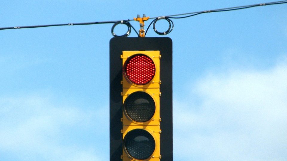 A yellow traffic signal hanging from a wire against a blue sky, its top lamp lit red