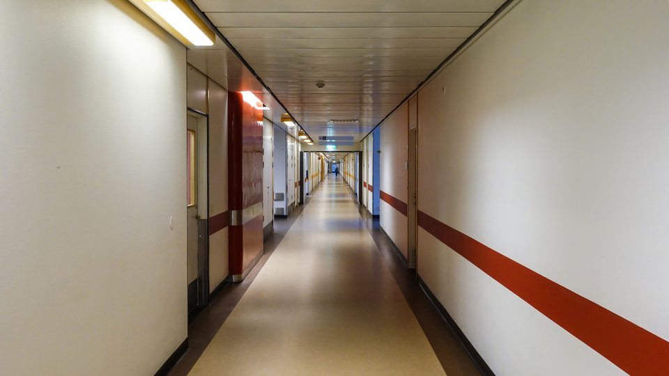 A long hospital corridor with white walls and a red stripe running along one side