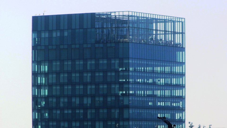 A blue glass office tower in Manchester under a bright sky